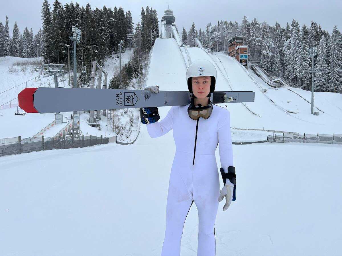 Timi Heiskanen m&auml;kihyppyrinteiden juurella sukset olallaan p&auml;&auml;ll&auml;&auml;n kokovalkoinen hyppypuku.