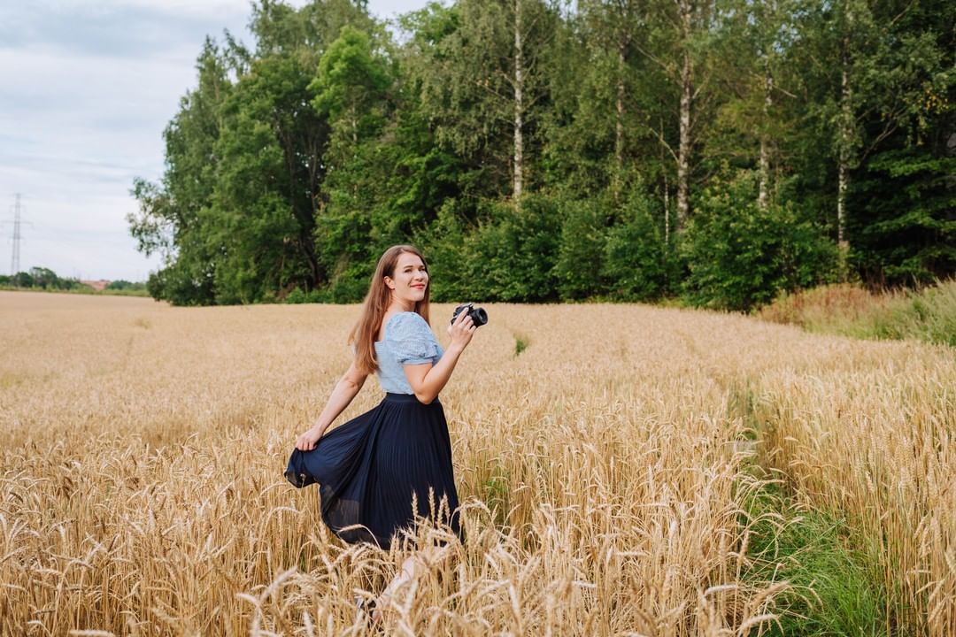 Linda poseeraa niittypellolla kädessään kamera
